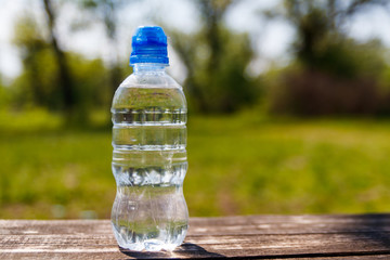 Plastic bottle with fresh drinking water on a wooden table on nature background