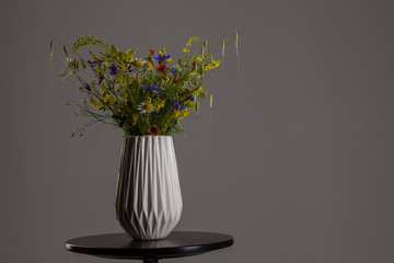 White vase with field flowers on a gray background