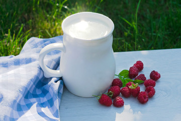  A cup of fresh milk and raspberry berries on a natural background of green grass.