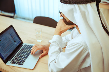 Arab saudi businessman working online with a laptop and tablet in his comfortable cabinet or...
