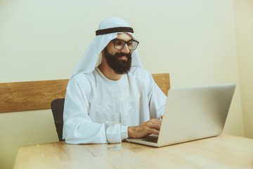 Arab saudi businessman working online with a laptop and tablet in his comfortable cabinet or...