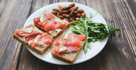 Wholemeal bread with salmon on white plate. Arugula and almond with lemon. Healthy sandwiches. Omega-3 for snack. Proper nutrition. Sport food.