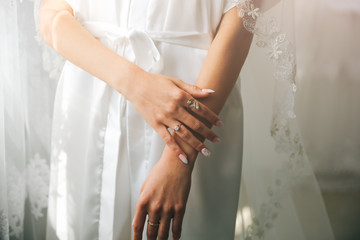 Bride in white clothes near the window. Beautiful manicure. Elegant nails. Golden rings. Wedding jewellery.