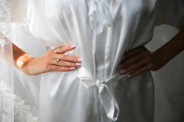 Bride in white clothes near the window. Beautiful manicure. Elegant nails. Golden rings. Wedding jewellery.