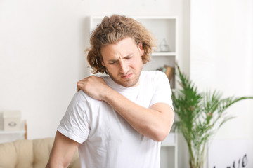 Young man suffering from pain in shoulder at home