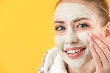 Beautiful young woman with facial mask on color background