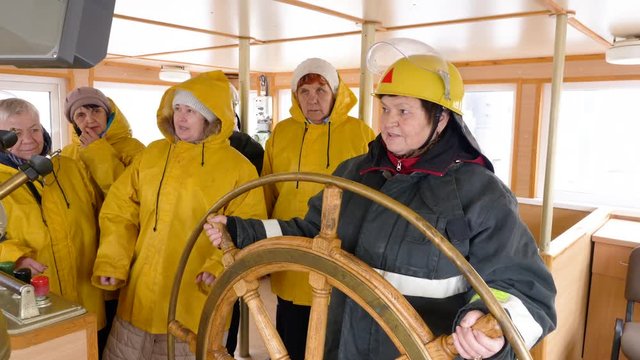 Female captain and ship crew in navigation bridge. Mature woman captain of fishing ship turning steering wheel and sailors standing on background. Unusual female professions