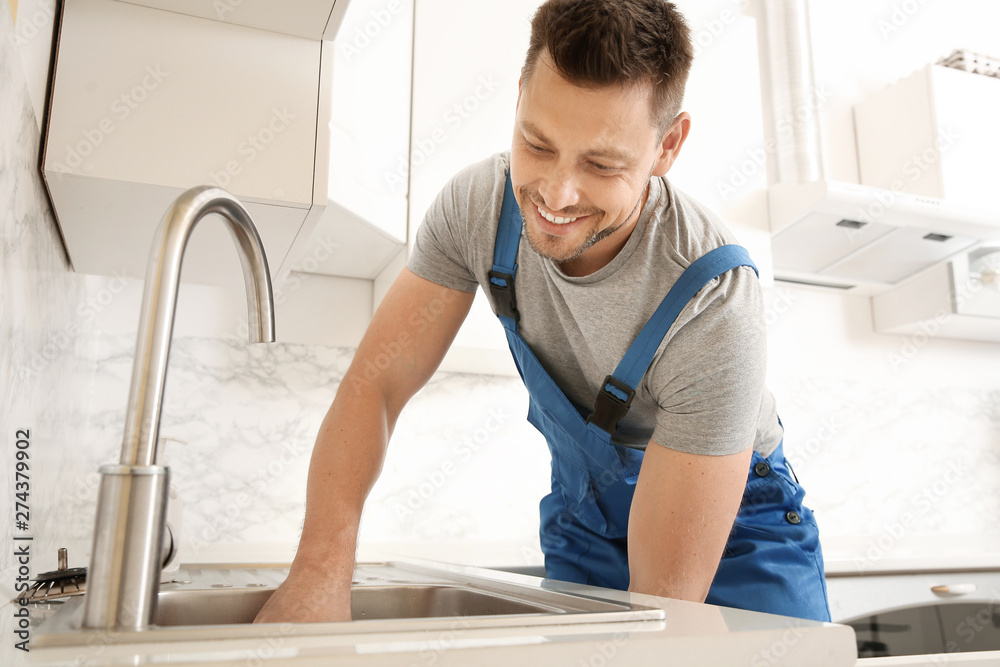 Poster plumber installing sink in kitchen