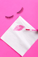 White paper napkin and lipstick kiss on it,faslse eyelashes on the pink background.Abstract concept of woman beauty