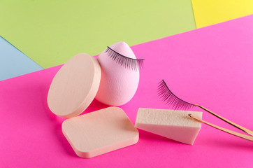 Closeup of cosmetic sponges, false eyelashes, tweezers on the colorful background