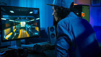 Excited Gamer Playing First-Person Shooter Online Video Game on His Powerful Personal Computer. Room and PC have Colorful Neon Led Lights. Young Man is Wearing a Cap. Cozy Evening at Home. © Gorodenkoff