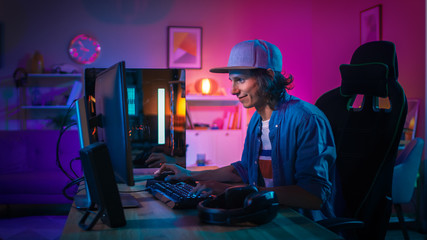 Professional Gamer Playing First-Person Shooter Online Video Game on His Powerful Personal Computer with Colorful Neon Led Lights. Young Man is Wearing a Cap. Living Room Lit with Pink Lamps. Evening. - obrazy, fototapety, plakaty