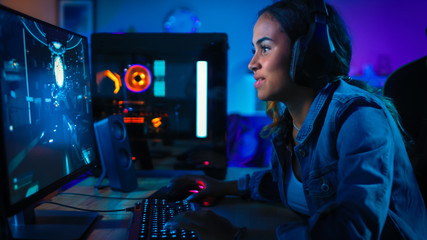 Pretty and Excited Black Gamer Girl in Headphones is Playing First-Person Shooter Online Video Game on Her Computer. Room and PC have Colorful Neon Led Lights. Cozy Evening at Home. © Gorodenkoff