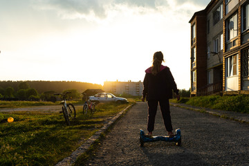 At sunset, a teen girl rides a hoverboard