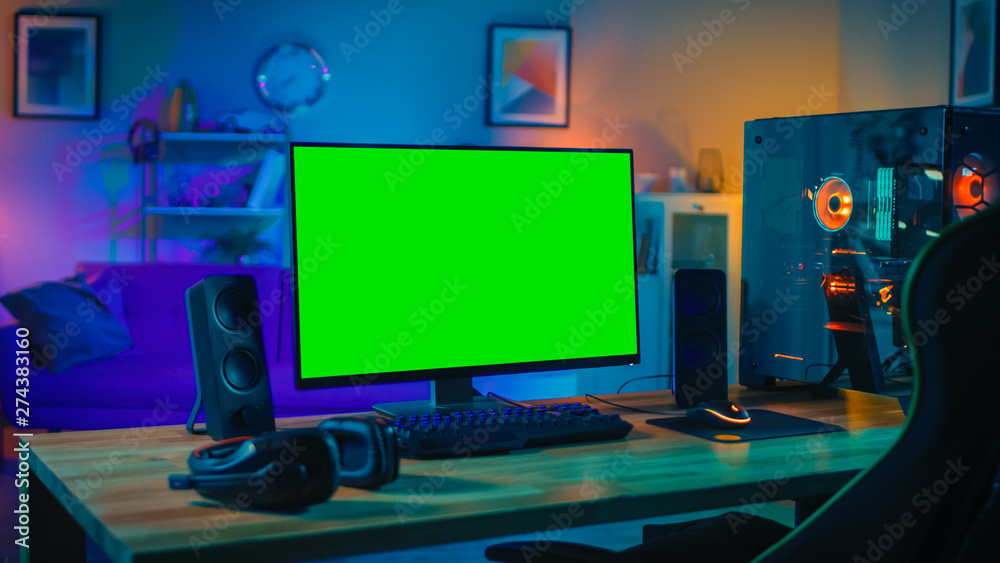 Wall mural Powerful Personal Computer Gamer Rig with Mock Up Green Screen Monitor Stands on the Table at Home. Cozy Room with Modern Design is Lit with Warm and Neon Light.