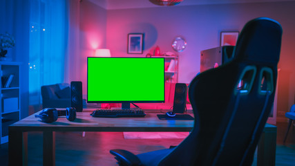 Powerful Personal Computer Gamer Rig with Mock Up Green Screen Monitor Stands on the Table at Home. Cozy Room with Modern Design is Lit with Pink Neon Light.