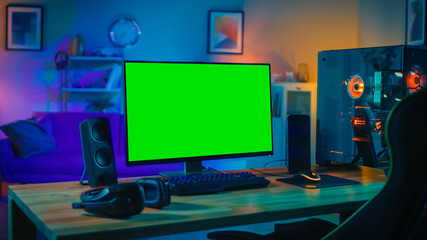 Powerful Personal Computer Gamer Rig with Mock Up Green Screen Monitor Stands on the Table at Home. Cozy Room with Modern Design is Lit with Warm and Neon Light. © Gorodenkoff