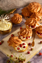 Eclairs custard cakes (shu, profiteroles) with strawberries on a dark background. Still life.