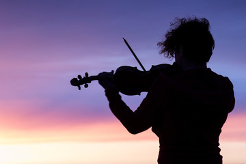 Silhouette of a woman with a violin at sunset.