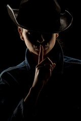 Silhouette of young unknown woman with finger on her lips and cowboy hat on black background