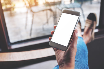 Mockup image of a woman holding white mobile phone with blank desktop screen while sitting in cafe