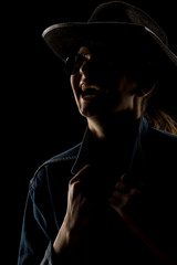 Fototapeta premium Silhouette of young unknown happy woman with kowboy hat and sunglasses on black background