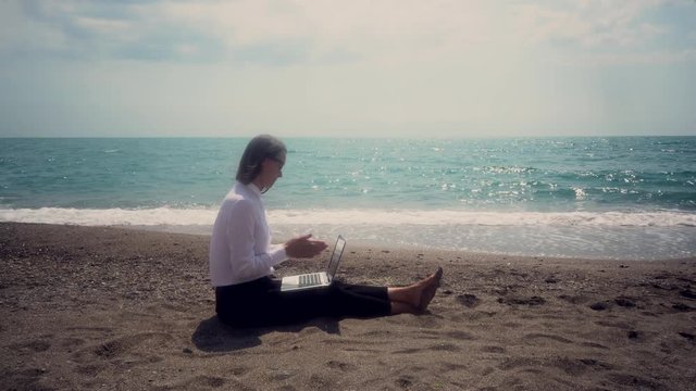 successful business woman with a mobile phone working in a laptop sitting on the beach. concept - vacation. toned image.