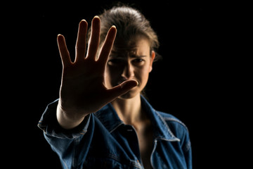 Fototapeta na wymiar Silhouette of young scared woman with syop hand on black background