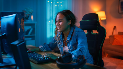 Beautiful Surprised and Excited Young Black Girl Watching Action Video on a Computer. She Has Dark Hair and Brown Eyes. Screen Adds Reflections to Her Face. Cozy Room is Lit with Warm Light.