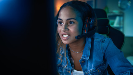 Excited and Focused Gamer Girl in Headset with Mic Playing Online Video Game on Her Personal Computer. She Talks to Other Players. Room and PC have Colorful Warm Neon Led Lights. Cozy Evening at Home. © Gorodenkoff