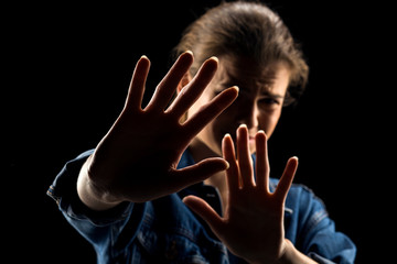 Silhouette of young scared woman with syop hand on black background