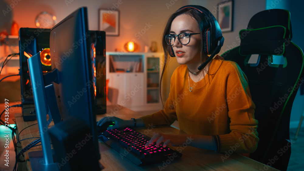 Wall mural excited gamer girl in headset with a mic playing online video game on her personal computer. she tal