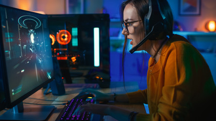 Pretty and Excited Gamer Girl in Glasses and Headset with a Mic Playing Shooter Online Video Game...