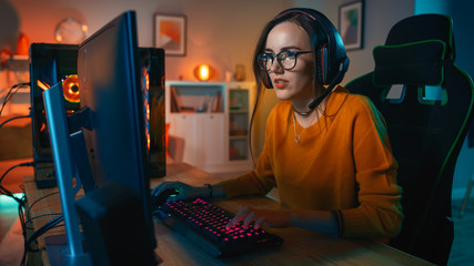 Excited Gamer Girl in Headset with a Mic Playing Online Video Game on Her Personal Computer. She...
