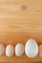 Chicken and goose eggs of different sizes in one line on the wooden background. Frame. Top view. Vertical. Concept we all are different