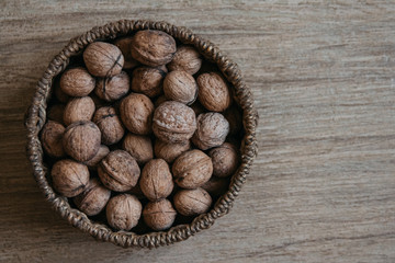 Walnuts in a round wicker basket on a wooden background. Top view. Copy, empty space for text.