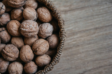 Walnuts in a round wicker basket on a wooden background. Top view. Copy, empty space for text.