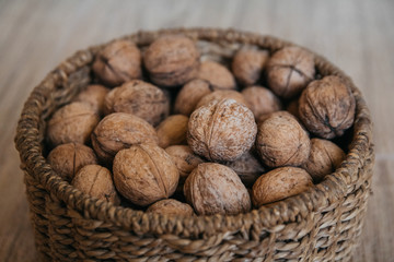 Walnuts in a round wicker basket on a wooden background. Close up.
