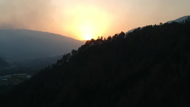 Drone flying over trees and mountains towards sunset