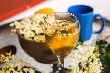 Glass with elderberry syrup, flowers, bowl, cup and lemon.