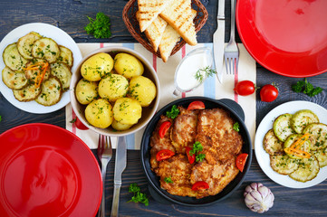 Boiled young potatoes, fried zucchini slices, schnitzels on a wooden table. Top view. Served table for family dinner, lunch. Rustic style