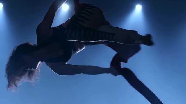 Graceful gymnast performing aerial exercise with red silk on blue light background. Slow motion. Closeup. 335