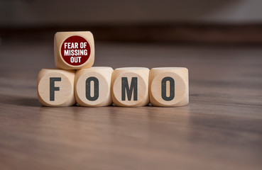 Cubes and dice with FOMO Fear of missing out on wooden background