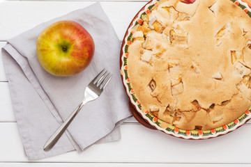Apple Charlotte pie with crispy crust in round baking dish on white wooden table with gray linen...