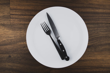 Empty white plate, spoon and knife isolated on wooden background. diet concept.
