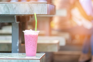 Iced milk pink tea in plastic cup  and green straw on marble chair.