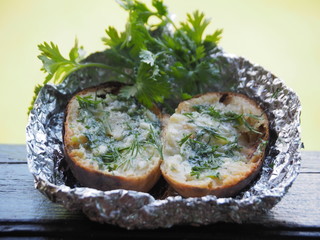 Potatoes in foil cooked in charcoal on a summer day in the garden. Baked potatoes with herbs and butter on a dark table close-up.