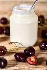Greek yoghurt with spoon, opened cherry with a ossicle, on a cherryes and brown wooden background