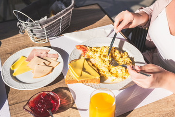 Woman have a breakfast with scrambled eggs, fresh orange  juice ham, cheese, bread and jam in a hotel restaurant.