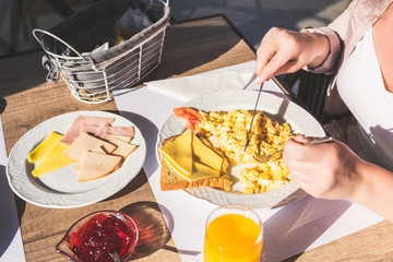Woman have a breakfast with scrambled eggs, fresh orange  juice ham, cheese, bread and jam in a hotel restaurant.